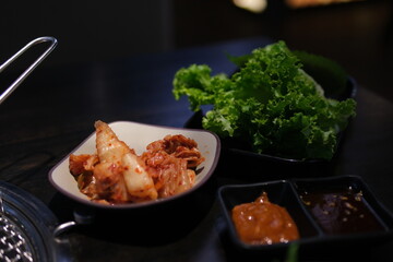 Spicy traditional lettuce kimchi in white bowl in table in kitchen with big copy space (kimchi: pickled and fermented vegetables, garlic, salt, ginger, chili peppers, etc). High quality photo
