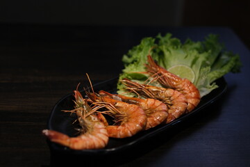 Grilled skewer shrimps and fresh vegetables served on black stony plate on wooden table. High quality photo