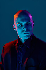 Handsome young bald man in dark shirt and jacket, looking to left with serious expression against...