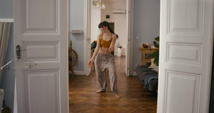 Girl in a yellow top and wide pants dances an impromptu contemporary dance on the floor of a house in a cozy apartment. Young girl funny improvised dance at home