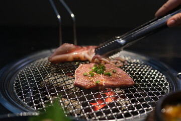 Close-up of hands masterfully flipping meats on a smoky grill, set against a blurred natural backdrop. High quality photo
