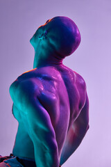 Back view of muscular young bald man posing shirtless, with sportive, strong, sweating body, on...