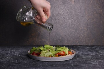 Woman pouring oil onto tasty salad at dark textured table, closeup