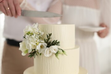 Married couple cutting delicious wedding cake with knife indoors, closeup