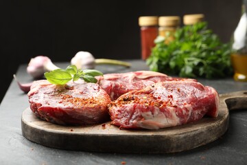 Raw steaks with spices and basil on grey table, closeup