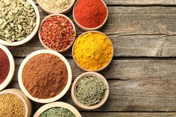 Different aromatic spices in bowls on wooden table, flat lay. Space for text