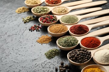 Many different spices in spoons on black table, closeup