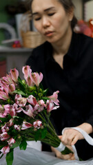 Fototapeta premium Female florist arranges delicate bouquet of pink alstroemeria flowers. Flower delivery. Small business concept