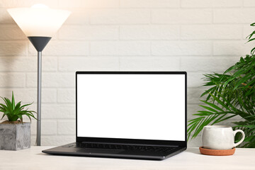 Fototapeta premium Laptop with white screen against white brick wall background