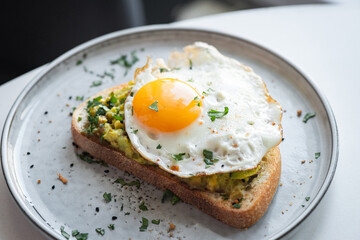 Breakfast toast with avocado and fried egg on a plate