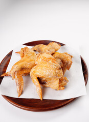 Fried chicken wings on paper towels on a wooden plate with a white background
