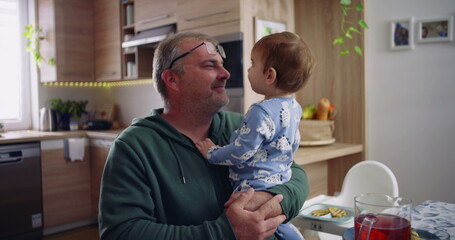 Father holding toddler and smiling, engaging in a playful and affectionate moment during family time in a cozy kitchen setting