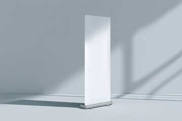 Blank retractable banner stand in a light-filled room.  Empty roll-up graphic display on a light gray floor. Soft shadows cast on the wall