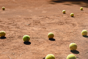 Tennis balls scattered on clay court during afternoon practice session