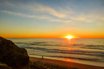 A vibrant sunset over the ocean, with the sun dipping below the horizon. Silhouettes of two people...