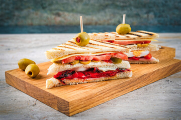 Traditional club toast sandwich with ham, cheese and egg served with vegetables as close-up on a wooden cutting board
