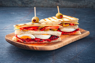 Traditional club toast sandwich with ham, cheese and egg served with vegetables as close-up on a wooden cutting board