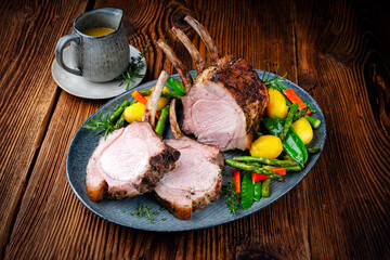 Juicy dry aged bone-in back rack of pork loin roast served as close-up with herbs and vegetable mix...