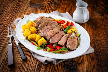 Traditional braised leg of lamb roast with vegetables and fried potatoes served as close-up in a classic design plate on a rustic wooden table