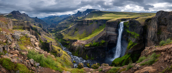 Majestic waterfall cascading down rocky cliffs, surrounded by lush greenery under a dramatic sky.