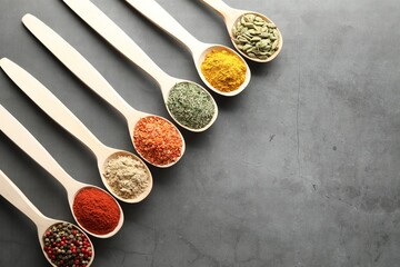 Many different spices in spoons on grey table, flat lay. Space for text