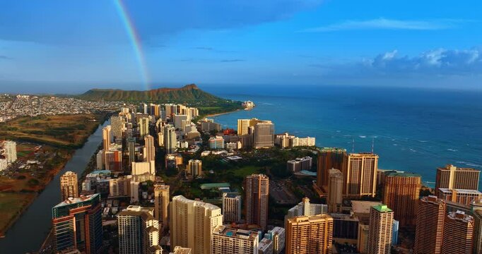 High-rise buildings of Waikiki are lit with bright sun. Rainbow falls into the Diamond Head Crater at backdrop. Hawaii, USA. Drone footage.