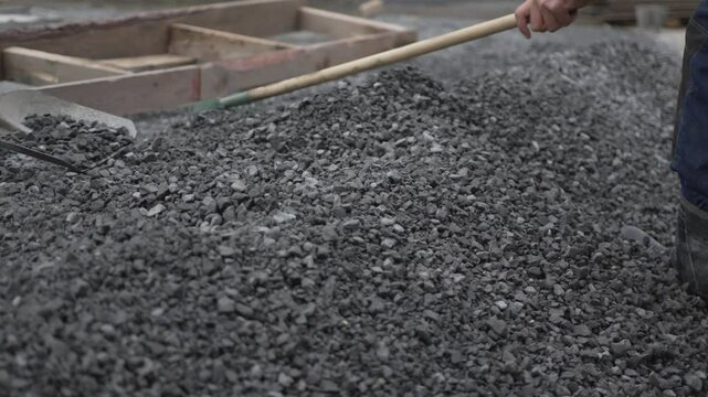 Workers spread and level gravel with shovel and rake. Wooden formwork marks construction area preparing foundation for new building