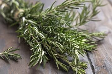 Fresh green rosemary sprigs on dark weathered wooden table closeup. Aromatic herb for culinary