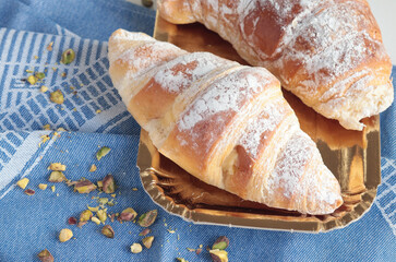 Croissant, brioche bun with powdered sugar and pistachio nuts on blue linen napkin. Breakfast and food. 