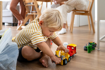 A young blonde child sits barefoot on a wooden floor, deeply engrossed in playing with colorful toy...