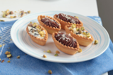 Sand dough tartlets with chocolate filling, pistachio nuts on white plate. Dessert for party, holiday. 