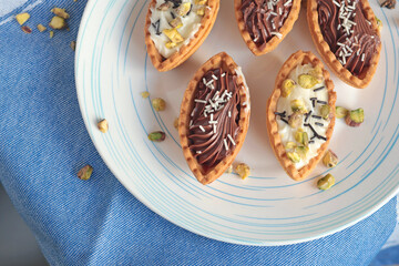Sand dough tartlets with chocolate filling, pistachio nuts on white plate. Dessert for party, holiday. 