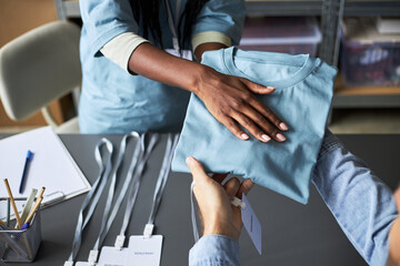 Distributing identification badges at work event with hands exchanging badges over table. Badges placed on surface with other office supplies while individuals are preparing