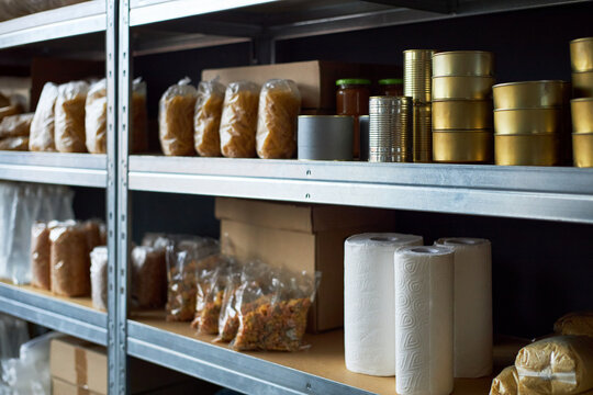 Neatly arranged shelves in well-stocked storeroom showing multiple supplies like canned food, pasta, paper towels, and jars prominently displayed in packages on metal racks