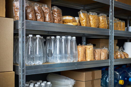 Shelves filled with packaged food and bottled water in a storage area. Supplies neatly organized on metal racks with various items including pasta and snacks