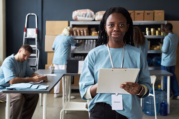 Portrait of African American woman wearing blue uniform, holding clipboard and smiling in work room...