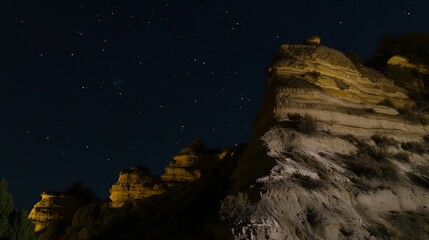 Nighttime landscape featuring layered rock formations under a starlit sky.
