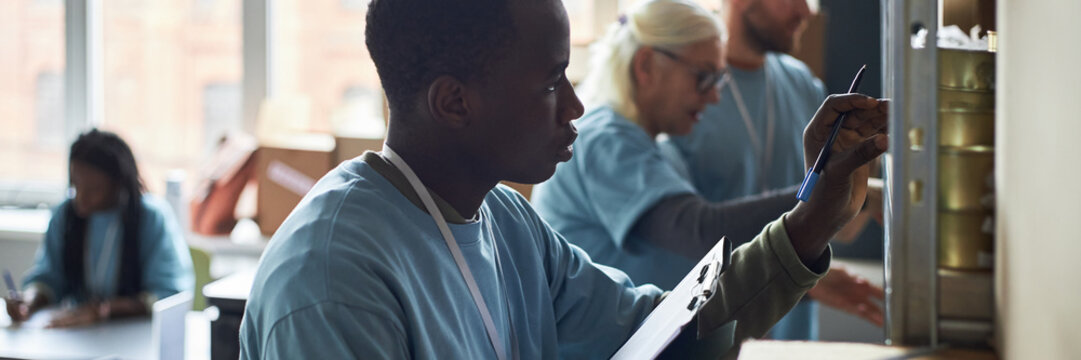 African American intern performing tasks in busy office environment with senior coworker supervising and other colleagues engaged in various activities in background