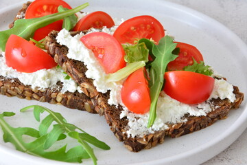 Open-faced sandwiches with rye bread, cottage cheese, tomatoes and arugula