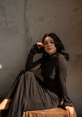 Naklejka premium Brunette in a black dress barefoot near a textured wall