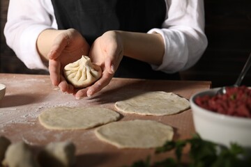 Woman making khinkali on table in kitchen, closeup