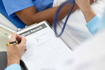 Doctor taking notes while patient explaining symptoms in hospital room. Doctor listens to a...