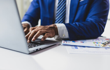 Businessman analyzing data and typing on laptop at work.