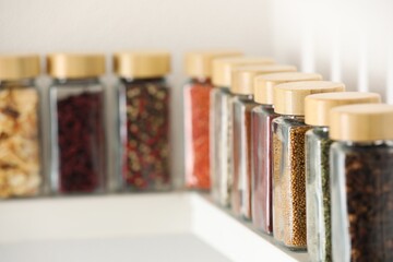 Different aromatic spices in jars on white shelf indoors, closeup. Space for text