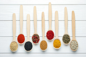Different aromatic spices in spoons on white wooden table, flat lay