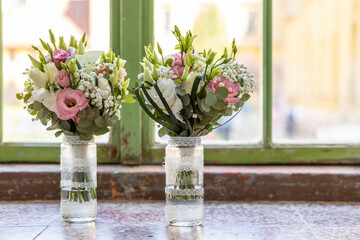 Two wedding bouquets resting on windowsill in decorated glass jars