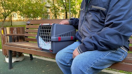 An elderly retired man holds a cat in a carrier. Pet transportation, traveling with a pet. A close friend of an elderly man