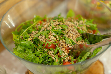 Fresh arugula salad with tomatoes and sunflower seeds being served in glass bowl