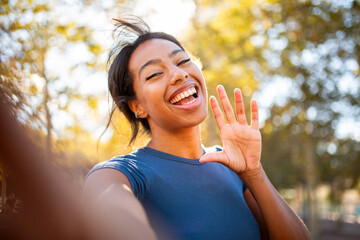 Playful selfie portrait of a young woman waving at the camera with a big smile