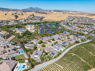 Aerial view of a suburban neighborhood with solar-paneled homes, swimming pools, and scenic rolling...
